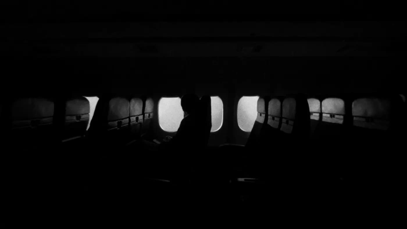 A row of lit windows down a darkened aircraft cabin at night, one passenger silhouetted.